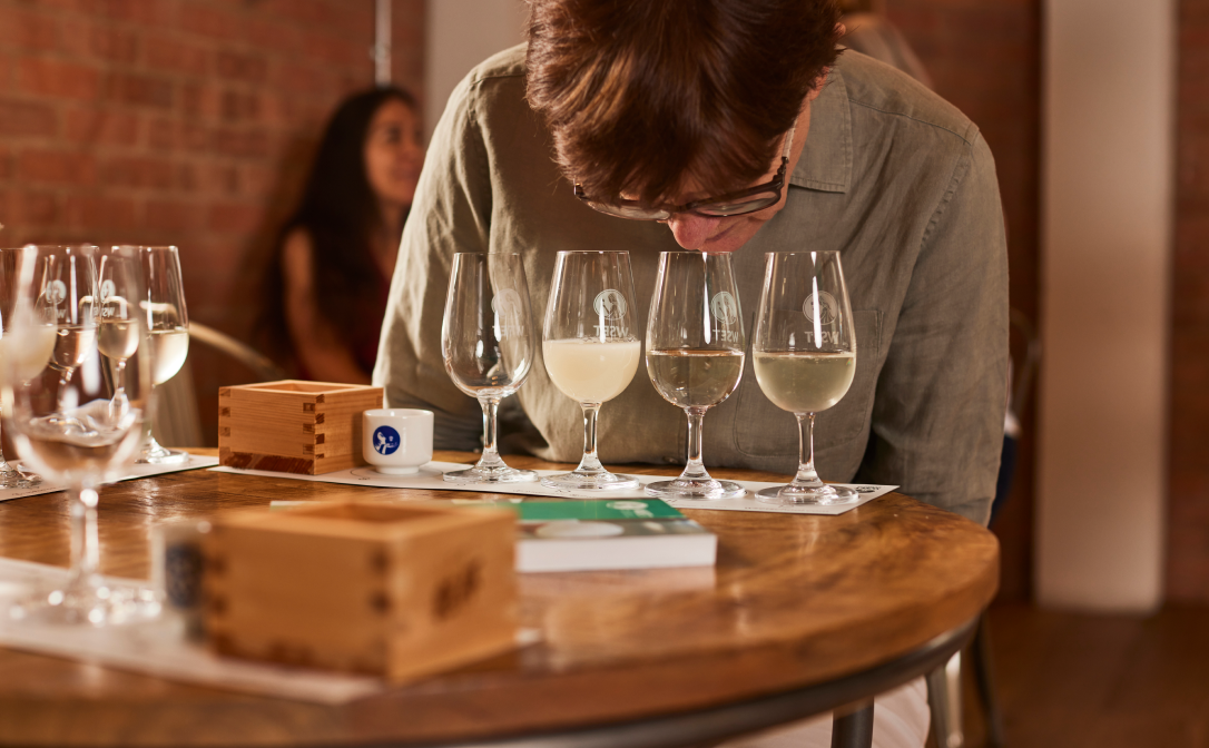 A student smelling a light coloured sake in a wine glass